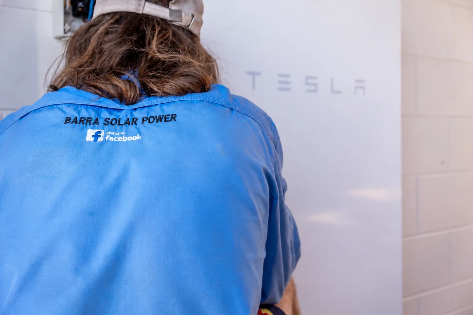 Townsville Solar Battery and Off-Grid | Barra Solar Power Townsville Barra Solar Power installer in a branded work shirt fitting a Tesla Powerwall battery in Townsville